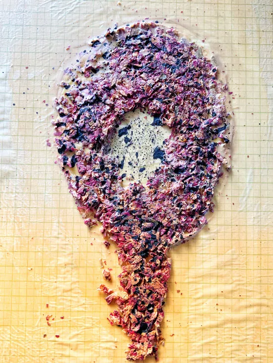 Crushed purple and pink flower petals pressed between plastic sheets on a gridded surface, textured and organic mood